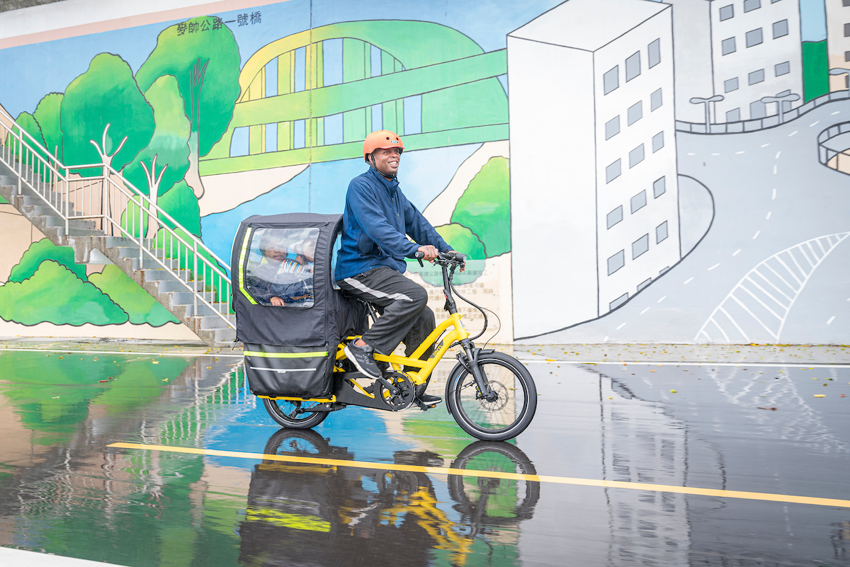 Dad riding GSD cargo bike with weather protection for kids