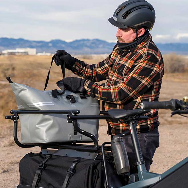 A man putting a WeatherTop Cooler bag into the Clubhouse cargo carrier installed on the rear rack of the bike.