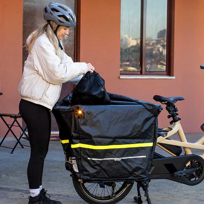 A woman putting her bag into the cargo carrier setup on the rear rack of the bike, which includes the Storm Box, the Clubhouse and Stow Decks.