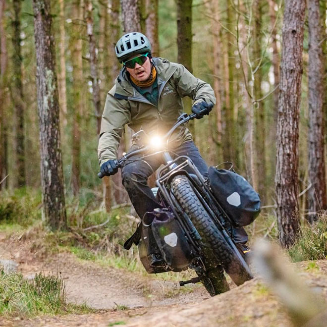 A man riding the Tern Orox cargo e-bike on the forest trail with two panniers loaded on the front rack.