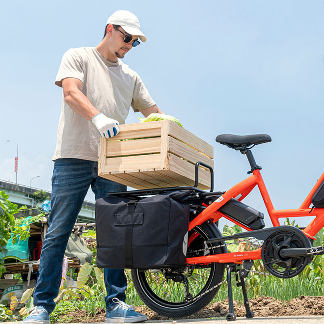 A man loads a wooden crate onto a red cargo bike equipped with a rear rack.