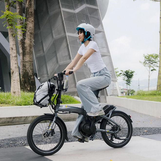 A woman wearing a white helmet rides a Vektron electric bike with a bag attached to the front.