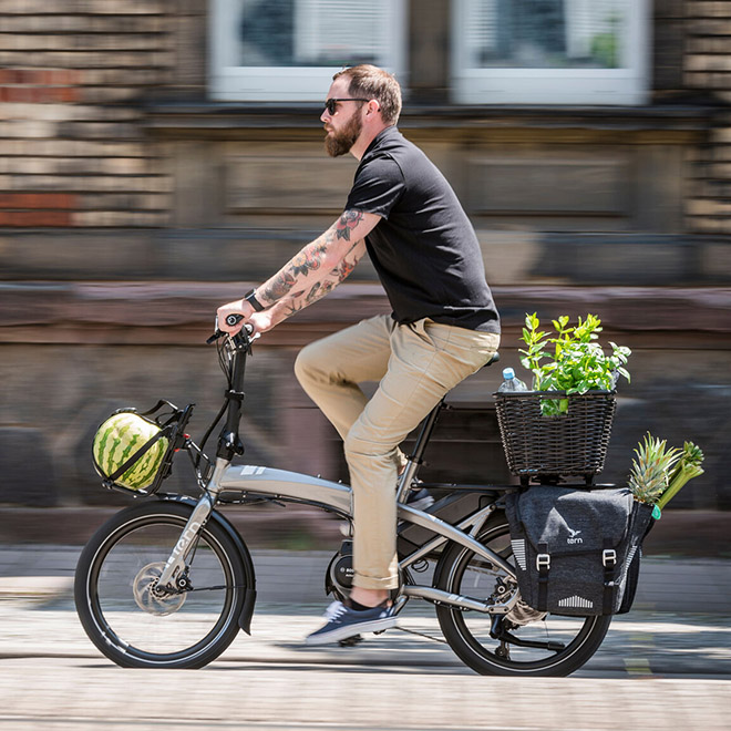 A man rides a Vektron electric folding bike equipped with a rear basket.