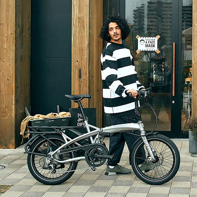 A man walking with a Vektron electric folding bike outside a café. 
