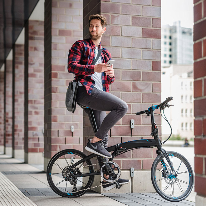 A man sitting on a Verge folding bike outside a brick building.