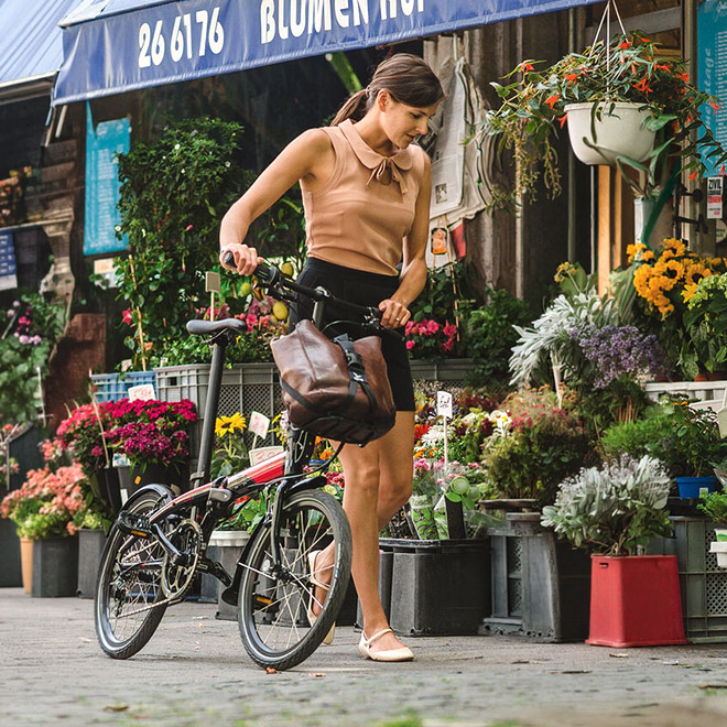 A woman walks with a Link folding bike outside a flower shop.