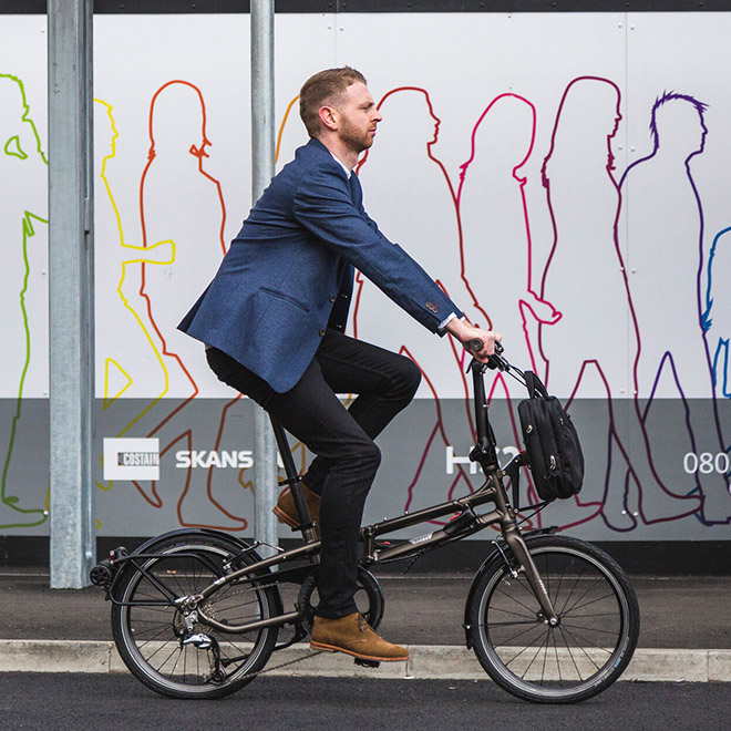 A man rides a BYB folding bike with a bag attached to the handlebars.