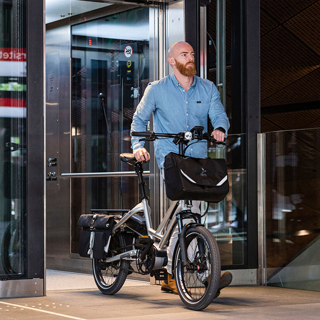 A man stands with a HSD electric cargo bike equipped with front and rear panniers. 