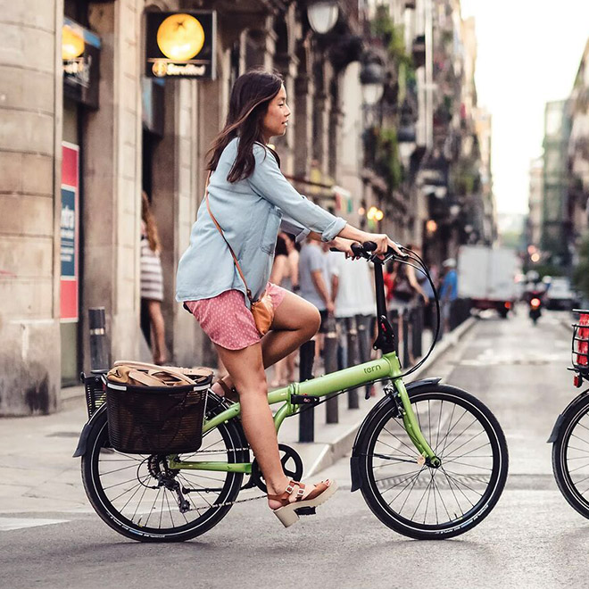 A woman rides a folding bike with a rear basket.
