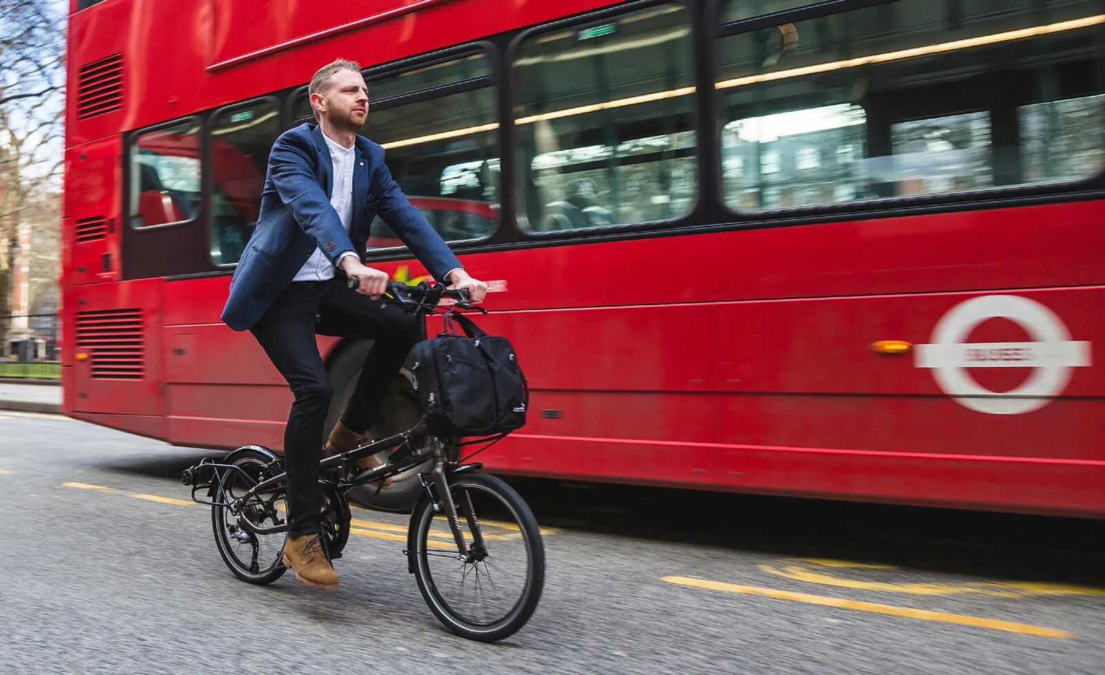 A business person riding a folding bike on the city road next to a bus