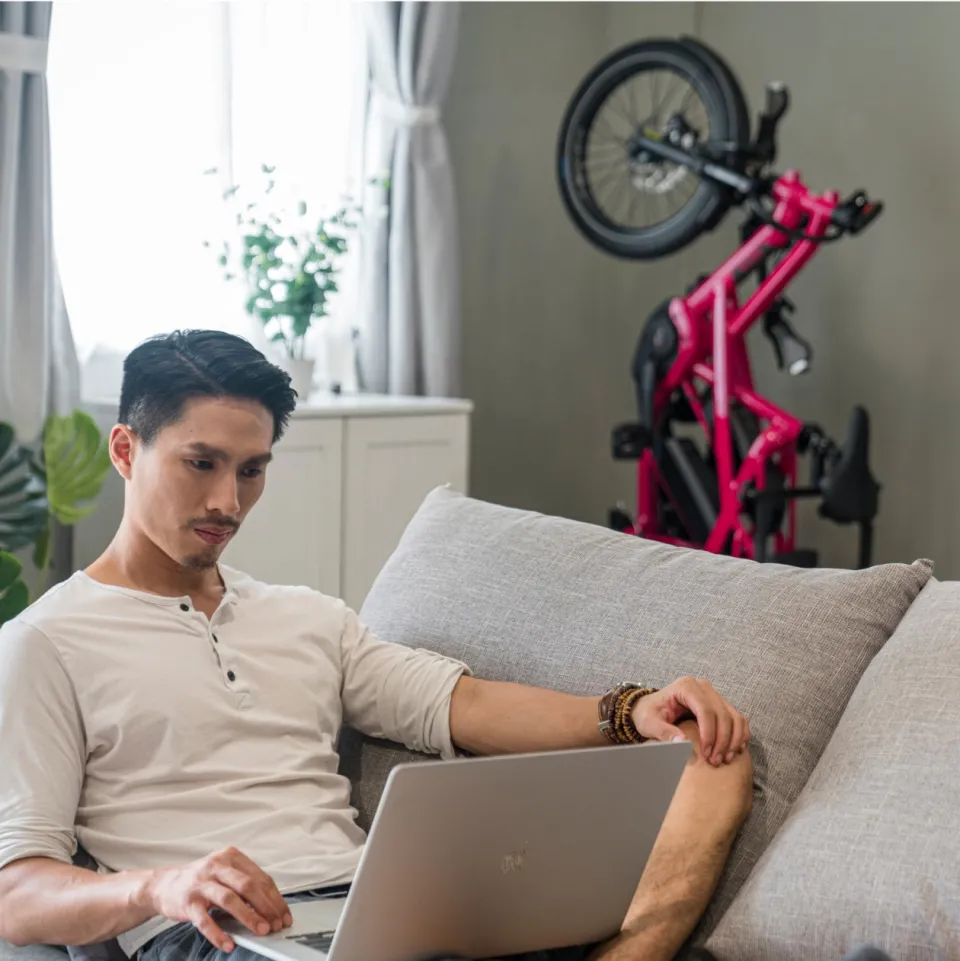 A men sitting in the sofa and a ruby red GSD bike park vertically in the corner