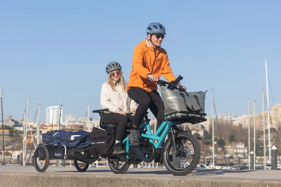 Couple riding a Tern GSD Gen 3 e cargo bike while carrying the waterproor WeatherTop Cooler and towing a trailer.