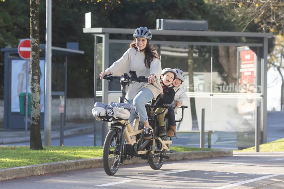 Family of three riding a Tern GSD Gen 3 cargo e bike, with two kids sitting in child seats inside the Clubhouse passenger rail.