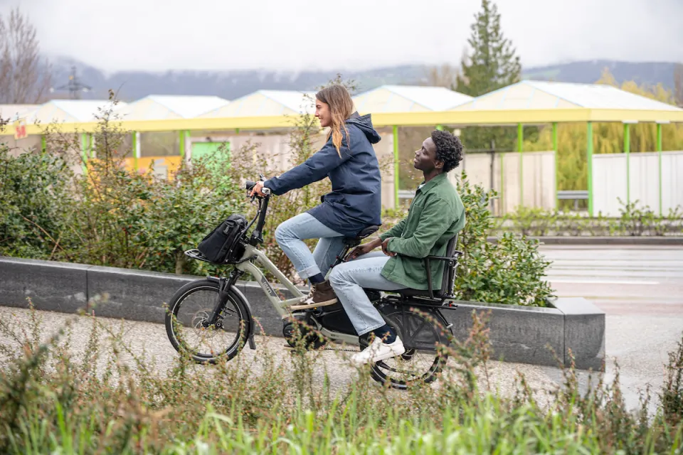 Woman riding a Tern HSD e-cargo bike while carrying an adult passenger on the rear rack