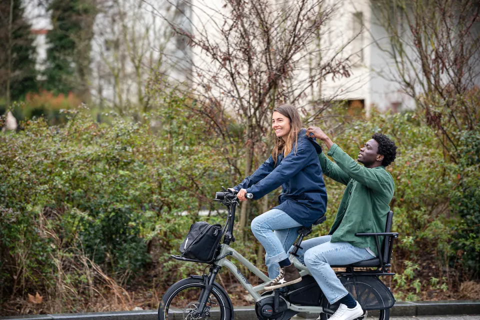 Woman riding a Tern HSD electric cargo bike with her partner sitting in the Captain's Chair passenger seat.