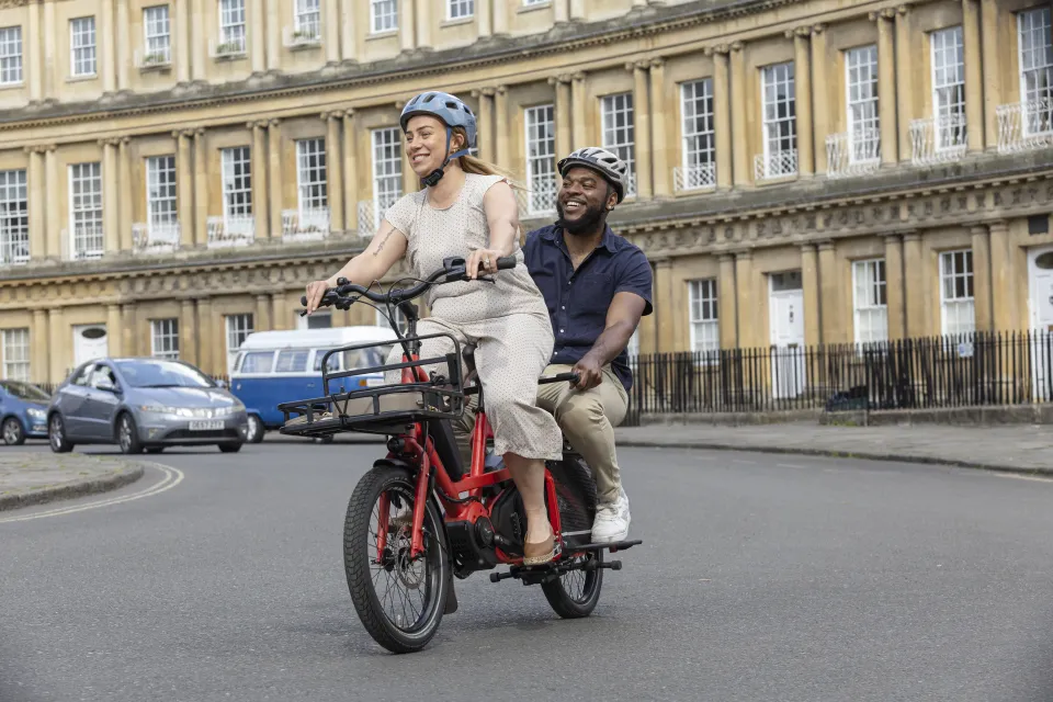 Woman riding the Tern Quick Haul Long family cargo bike with her partner in the Captain's Chair passenger seat.