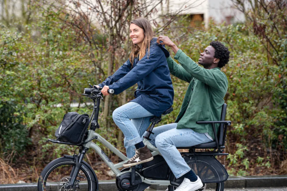 Woman riding a Tern HSD e-cargo bike with her partner sitting in the Captain's Chair passenger seat.