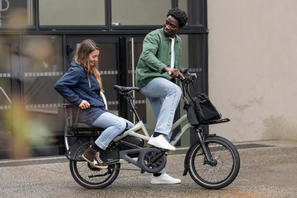 Man riding a Tern HSD Gen 2 e cargo bike with an adult passenger on the rear rack.