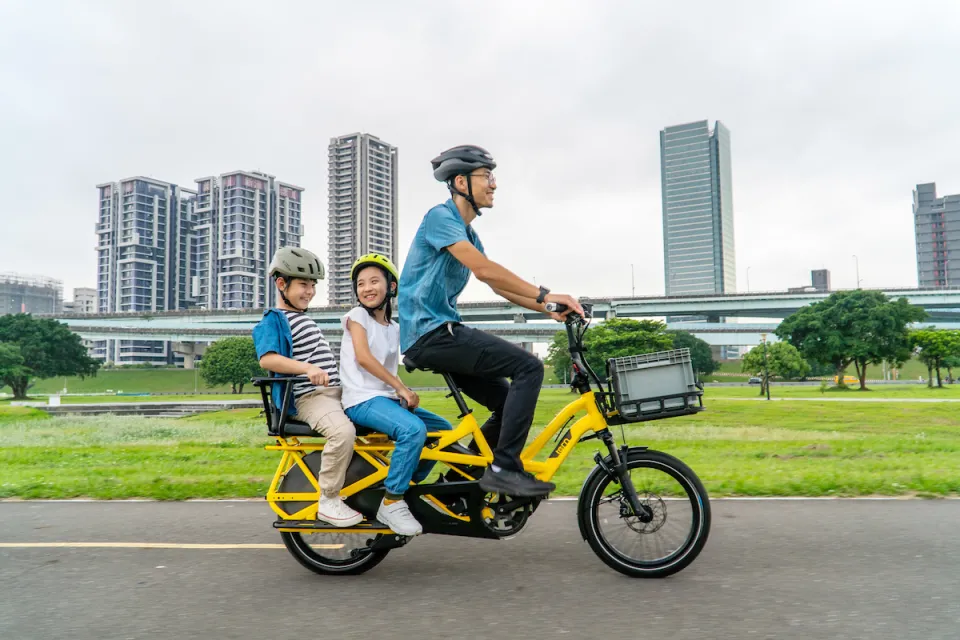 Family of three riding a Tern GSD Gen 2 cargo ebike equipped with the Captain's Chair and Sidekick Handle passenger accessories.