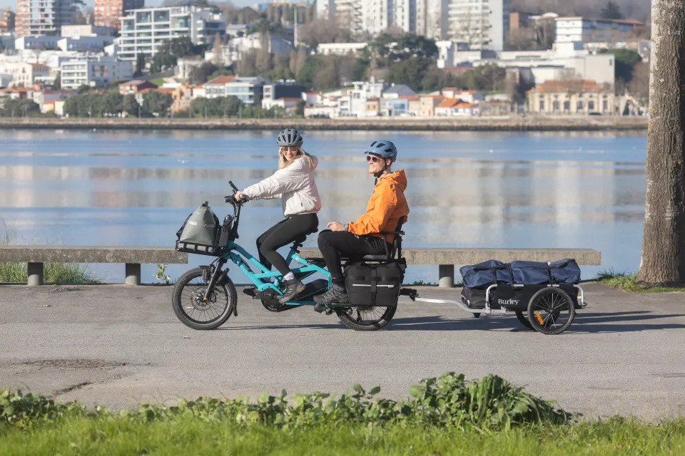 Couple riding on a Tern GSD Gen 3 cargo ebike while towing a Burley bike trailer.