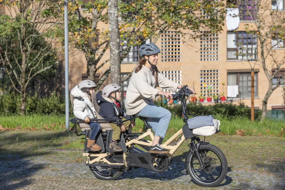 Woman carrying her two kids on a Tern GSD Gen 3 electric cargo bike. The kids are seated in child seats in the Clubhouse passenger rail.