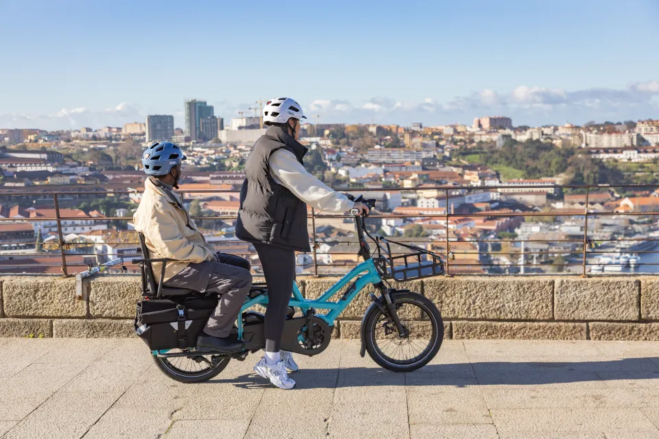Father and daughter on a Tern GSD Gen 3 cargo e bike; standing still on a bridge as they enjoy a city view.