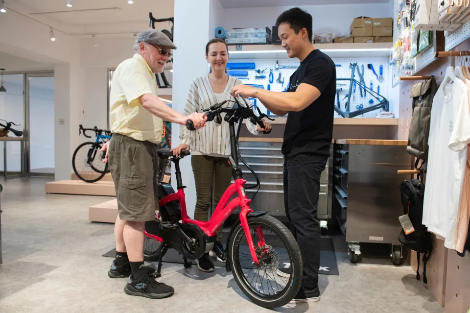A dealer demonstrating the features of a Tern NBD low-step ebike to a senior couple in the bike shop.