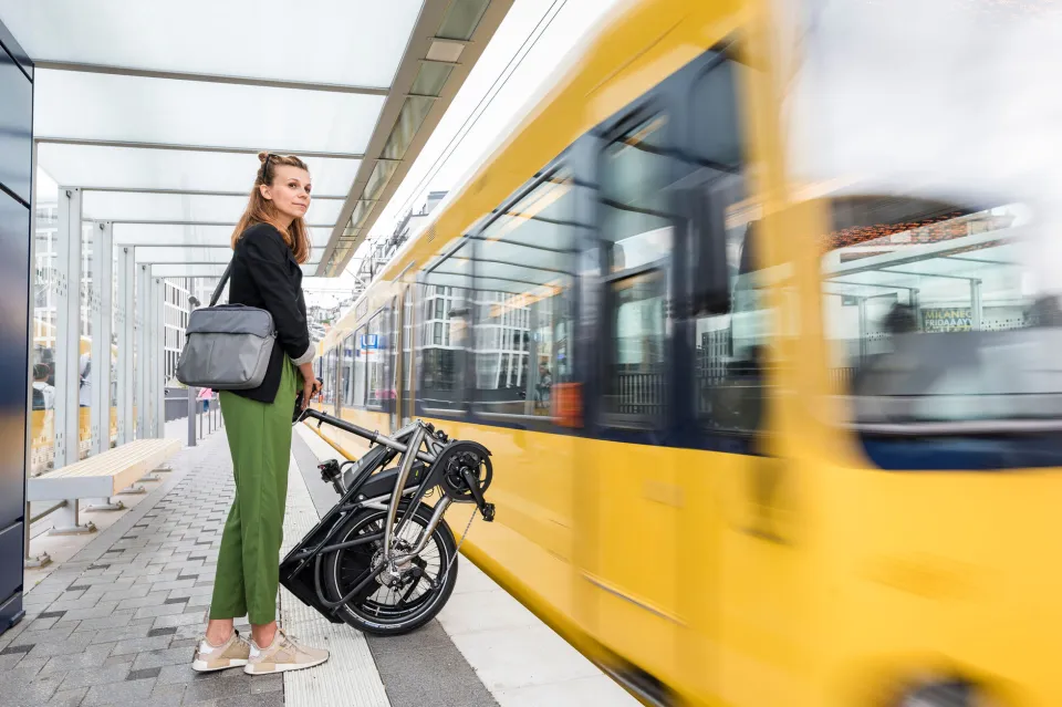 A woman holding an upright folded Tern Vektron e-bike waiting for a train.