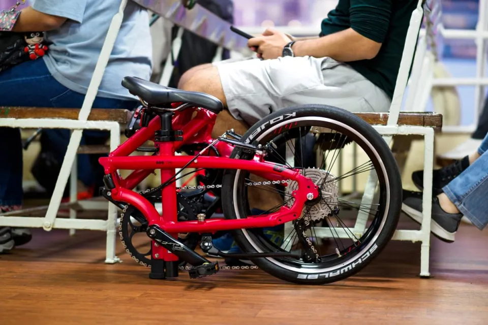 A folded Tern BYB folding bike kept next to the rider's seat in an indoor venue.