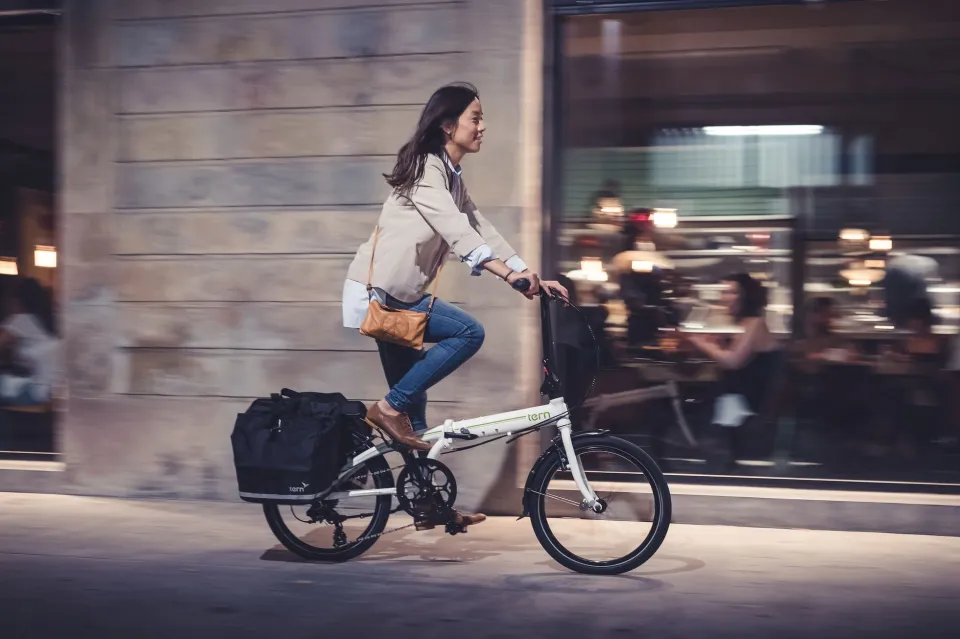 A young woman riding a Tern Link C8 folding bike with two panniers on her rear rack. 