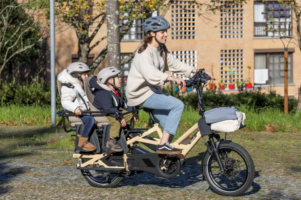 A mom riding a Tern GSD e-cargo bike with two kids on the back, protected by the enclosed Clubhouse.