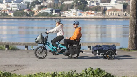 A woman riding a Tern GSD Gen 3 e-cargo bike, towing a trailer and with her partner in the passenger seat