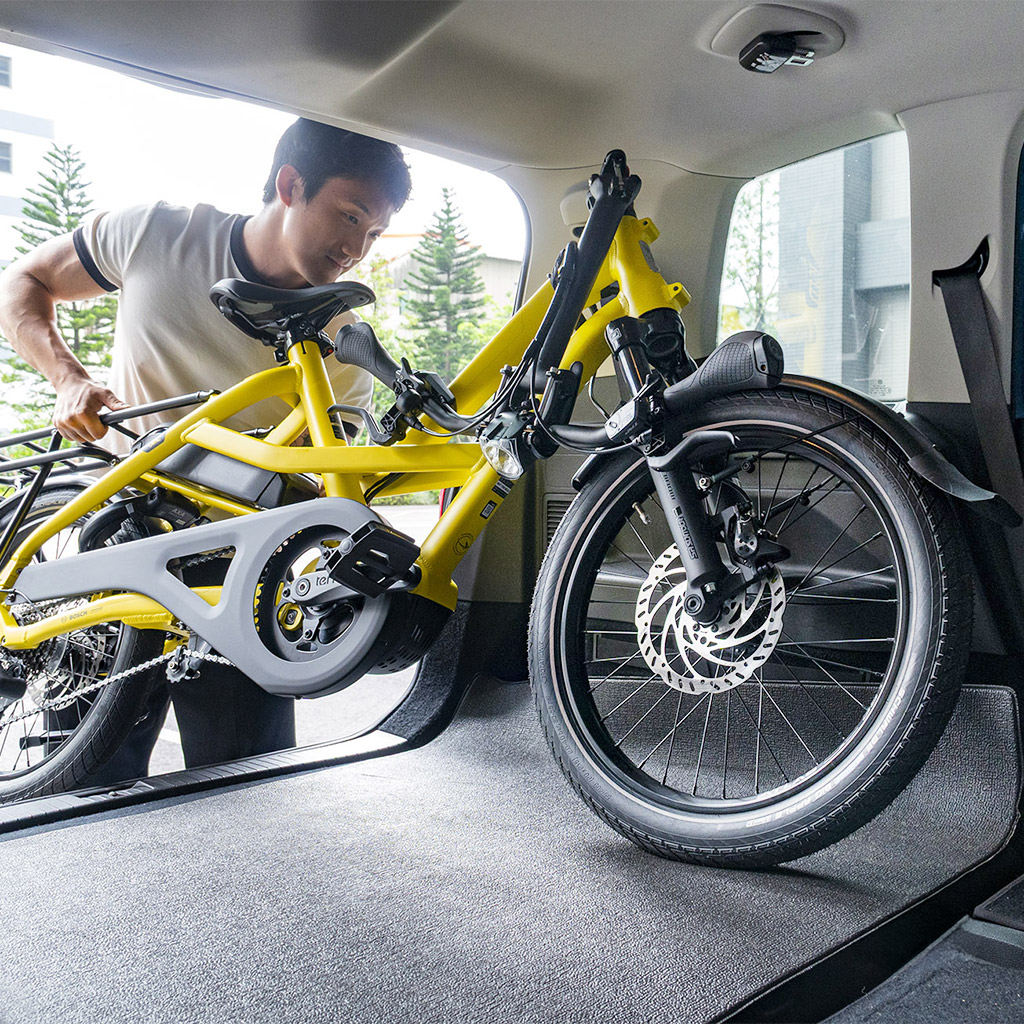 Een man laadt een plat opgevouwen Tern HSD e-cargobike in de kofferbak van een auto.