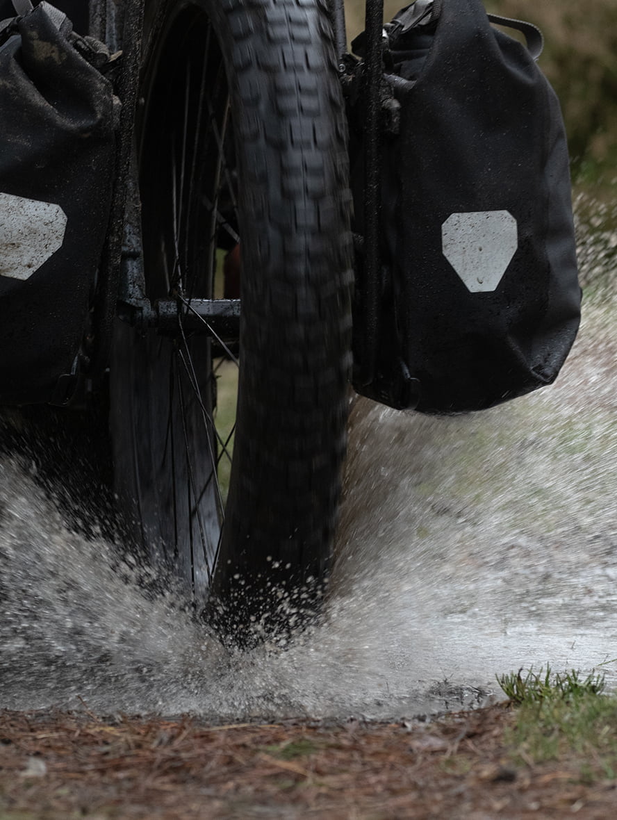The tire rides through a puddle, splashing water